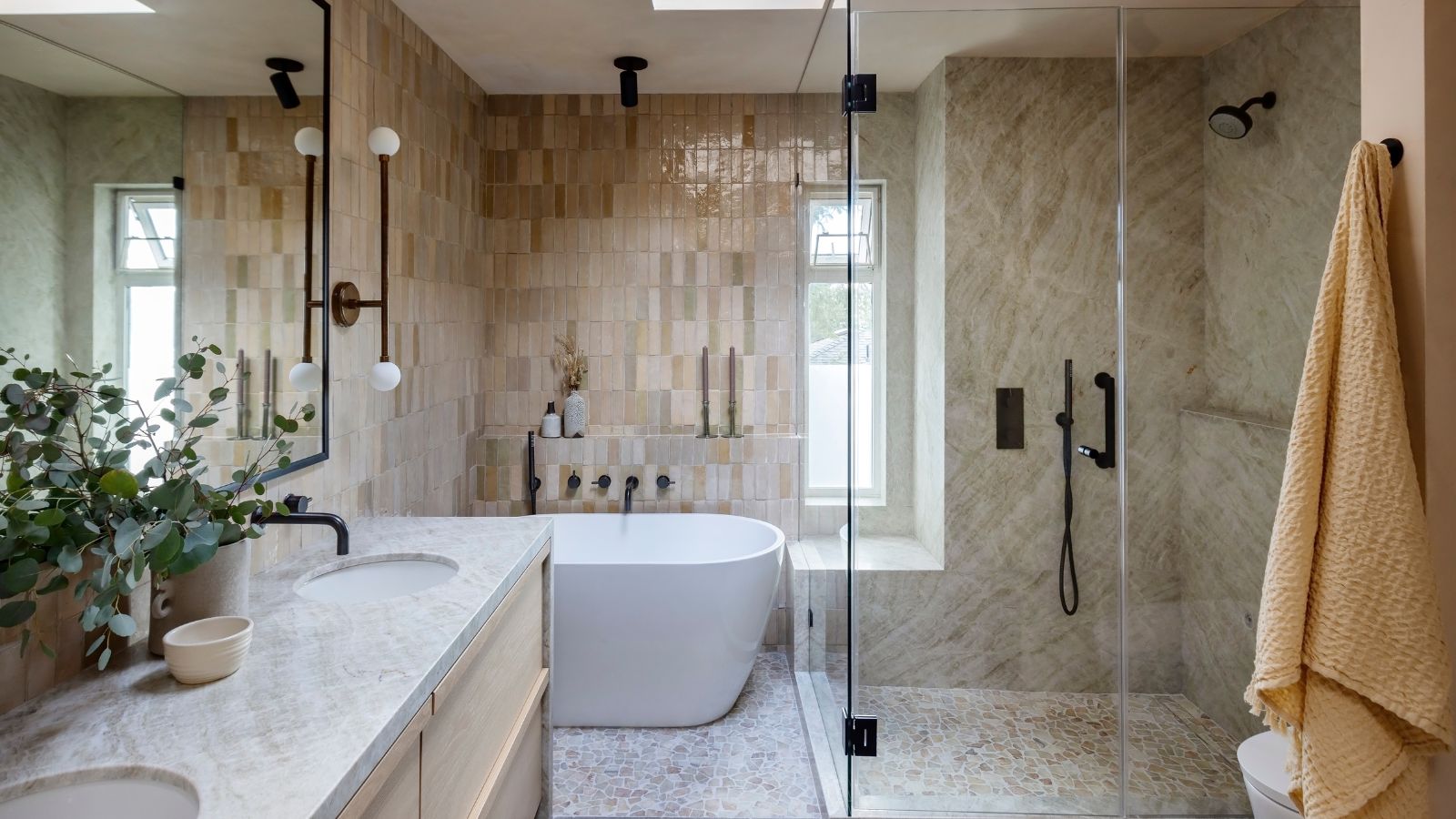A neutral bathroom with wall tiles, a wooden vanity, and a glass shower screen