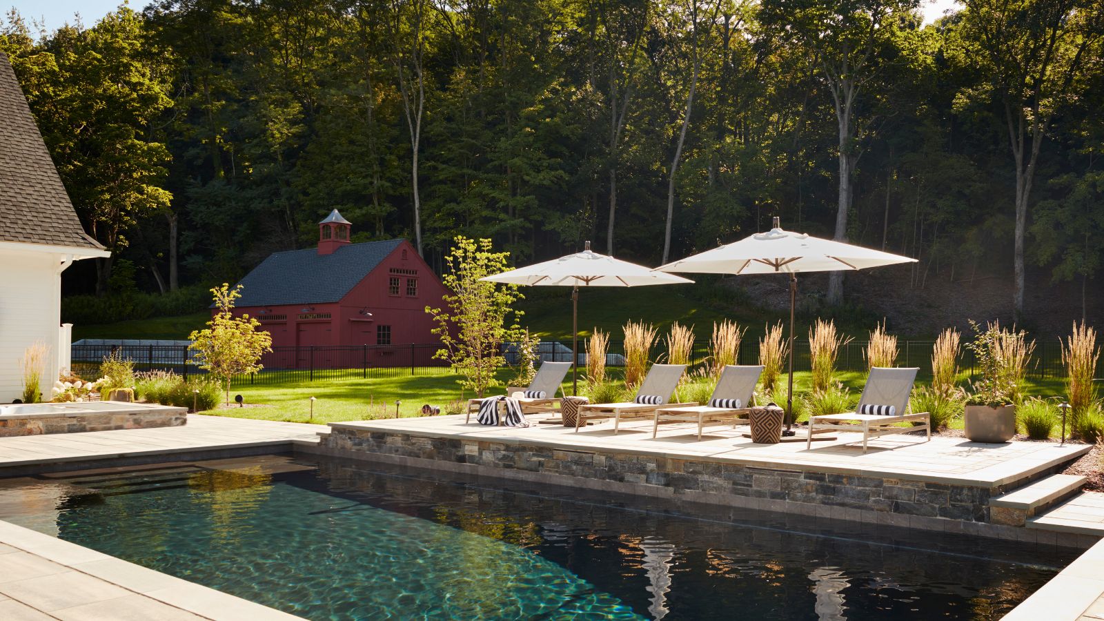 large outdoor pool area with a red barn style pool house, patio loungers with striped cushions and white patio umbrellas