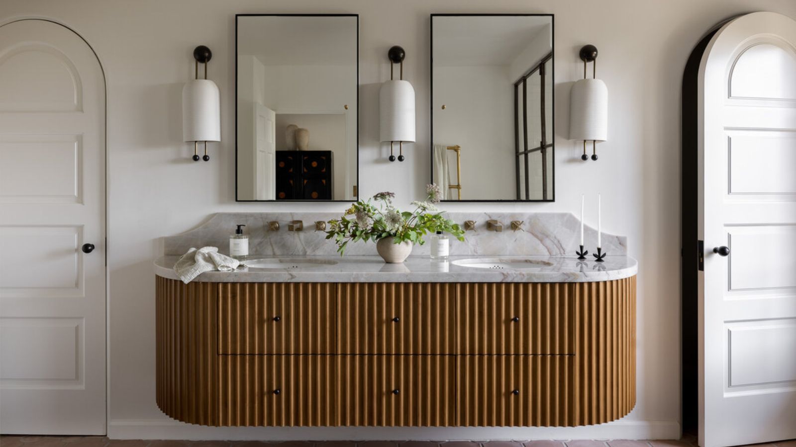 A bathroom with fluted wood vanity, marble countertop, black rectangular mirrors, and statement wall sconces