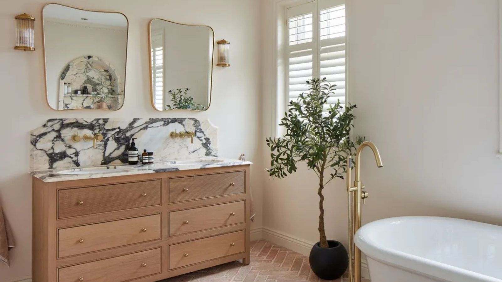 Cream bathroom with double wooden vanity and marble top with two gold mirrors hung above