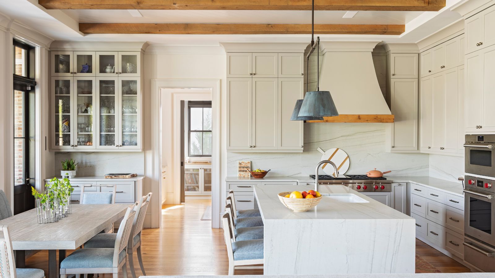 A large neutral kitchen with custom cabinets and range hood, a large island, and a small dining space