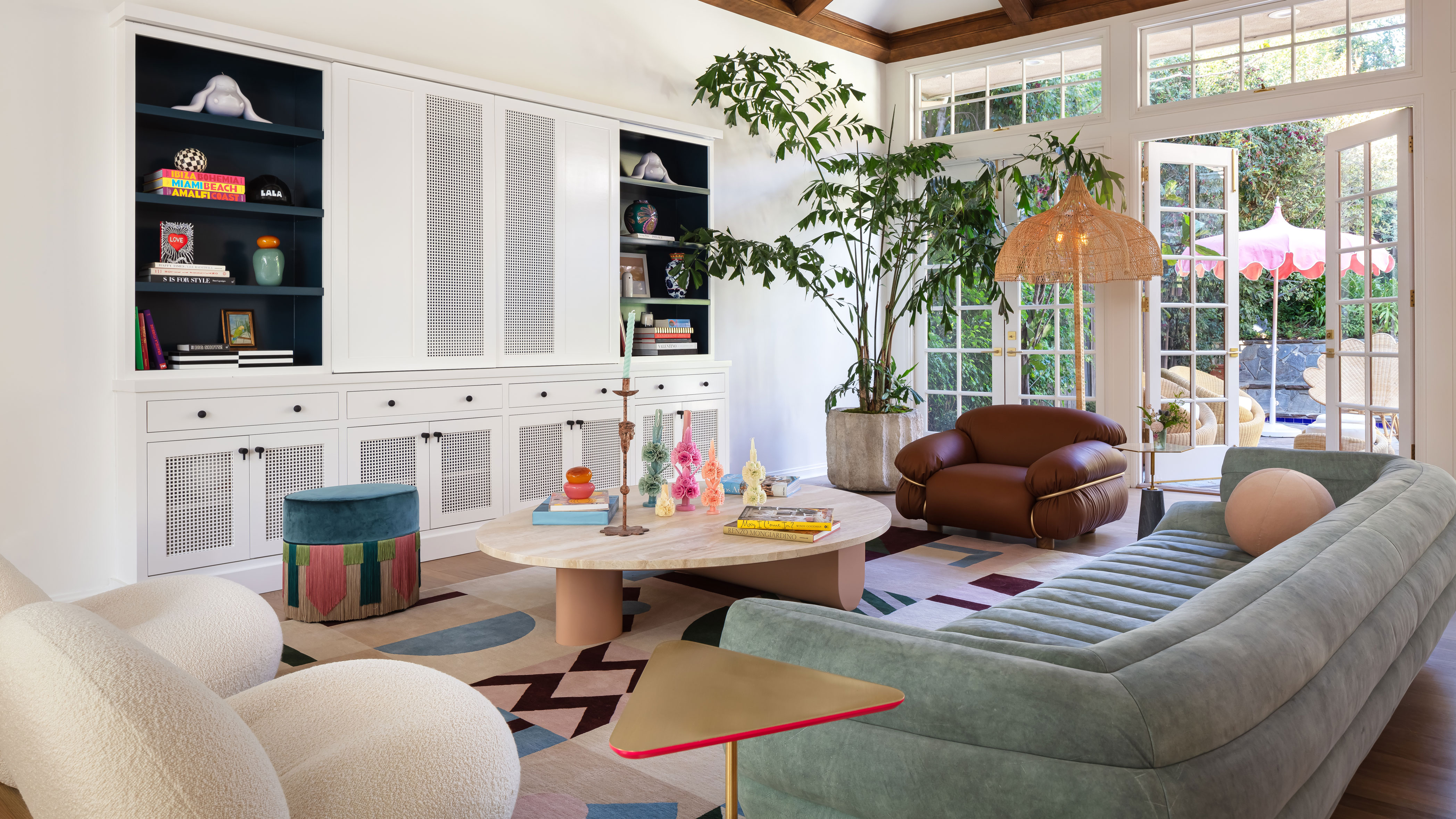 LALA Reimagined designed living room with white walls, green sofa, white armchair, round wooden coffee table, brown leather armchair and colorful rug with built-in storage