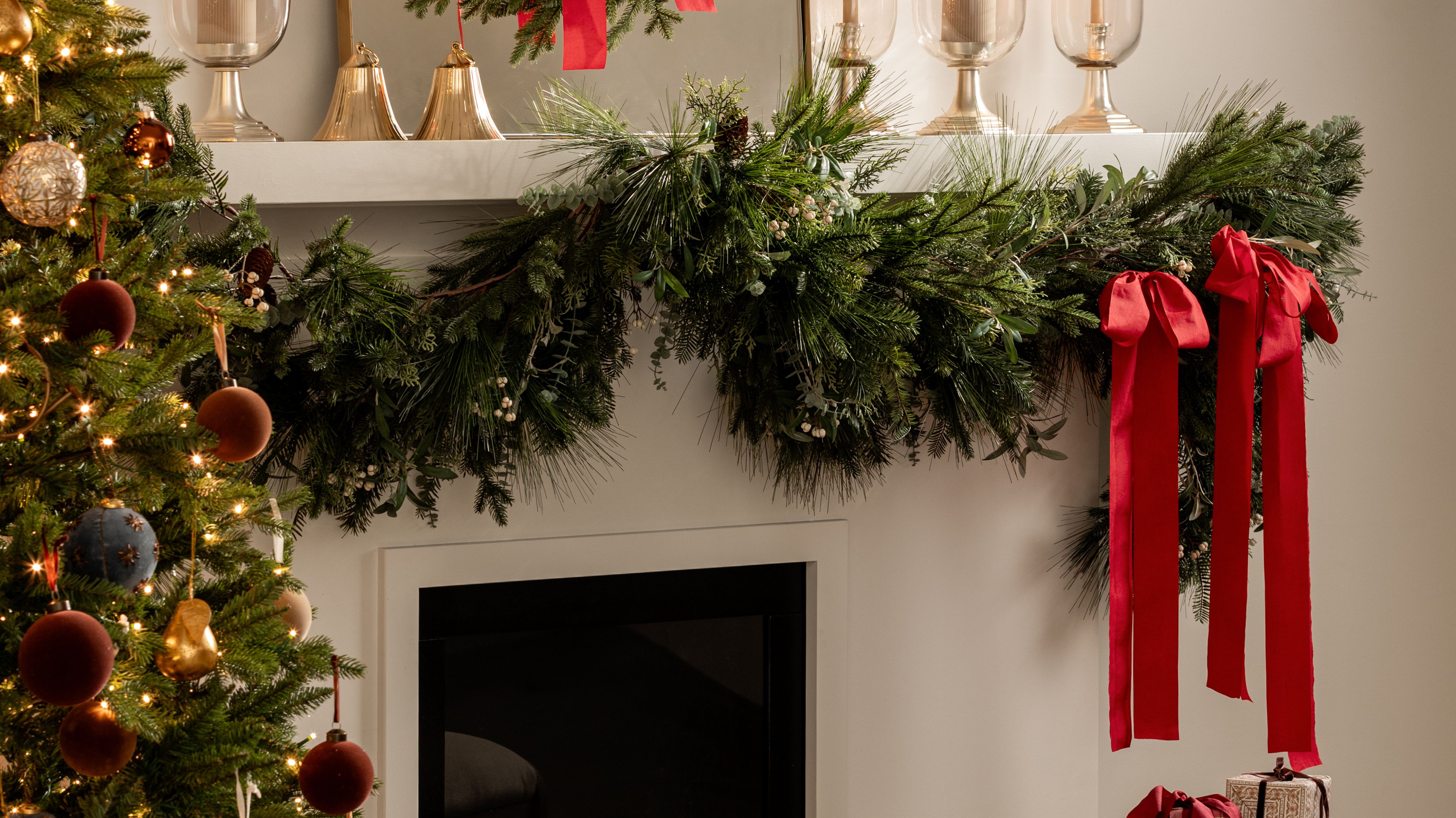 Festive holiday mantle styled with evergreen garland, brass bells, and red bows 