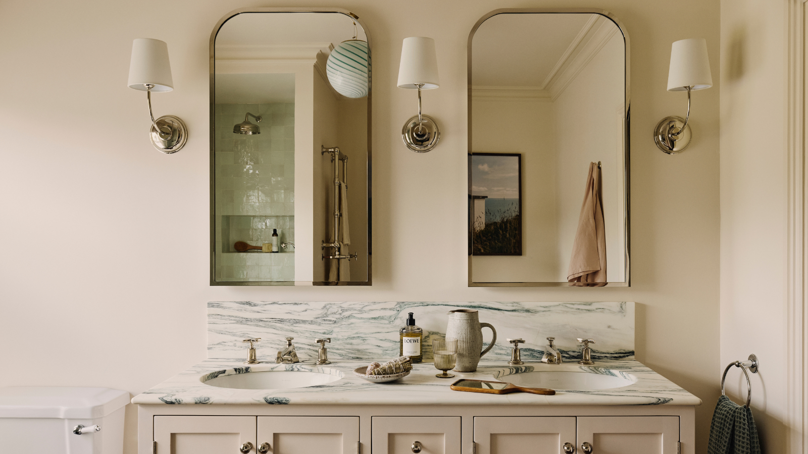 a bathroom with a double vanity, two mirrors, three wall sconces, and various bathroom necessities on the countertop